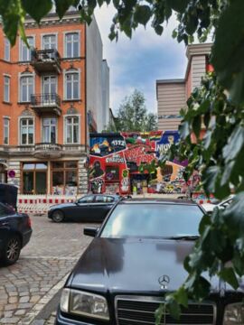 Parkende Autos (Mercedes) vor mit Grafittis bemaltem Haus.